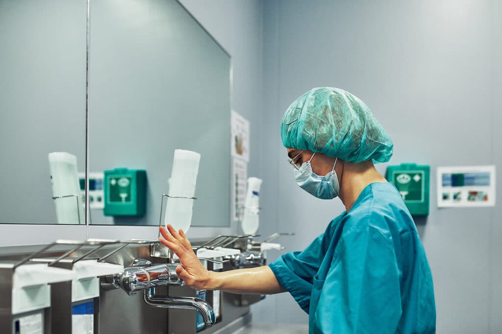 Fiatal nő egészségügyi védőfelszerelésben, maszkban sterilizáló műszerekkel sterilizál. Fertőtlenítő-sterilező képzés, Pannon KIncstár szakmai cikk